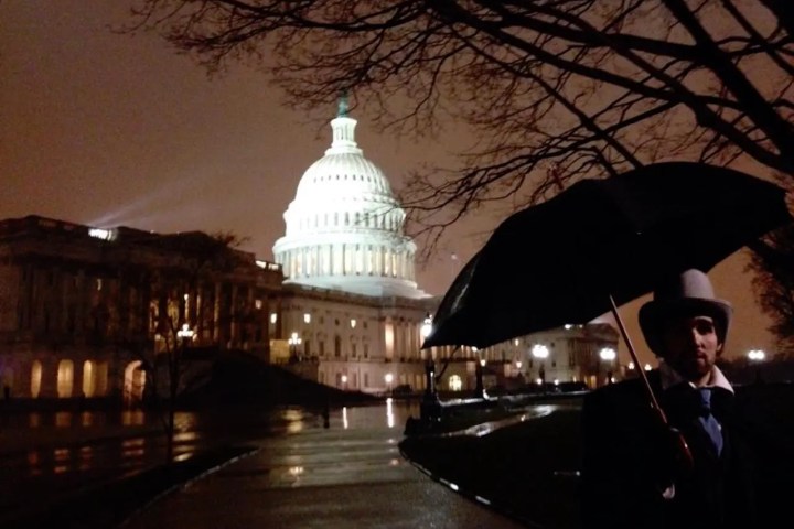 Person with umbrella near illuminated Capitol building at night.