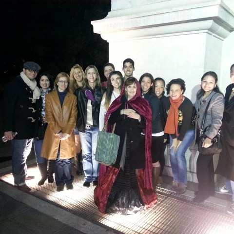 Group of 13 people posing under a lit area at night, by a large white structure.
