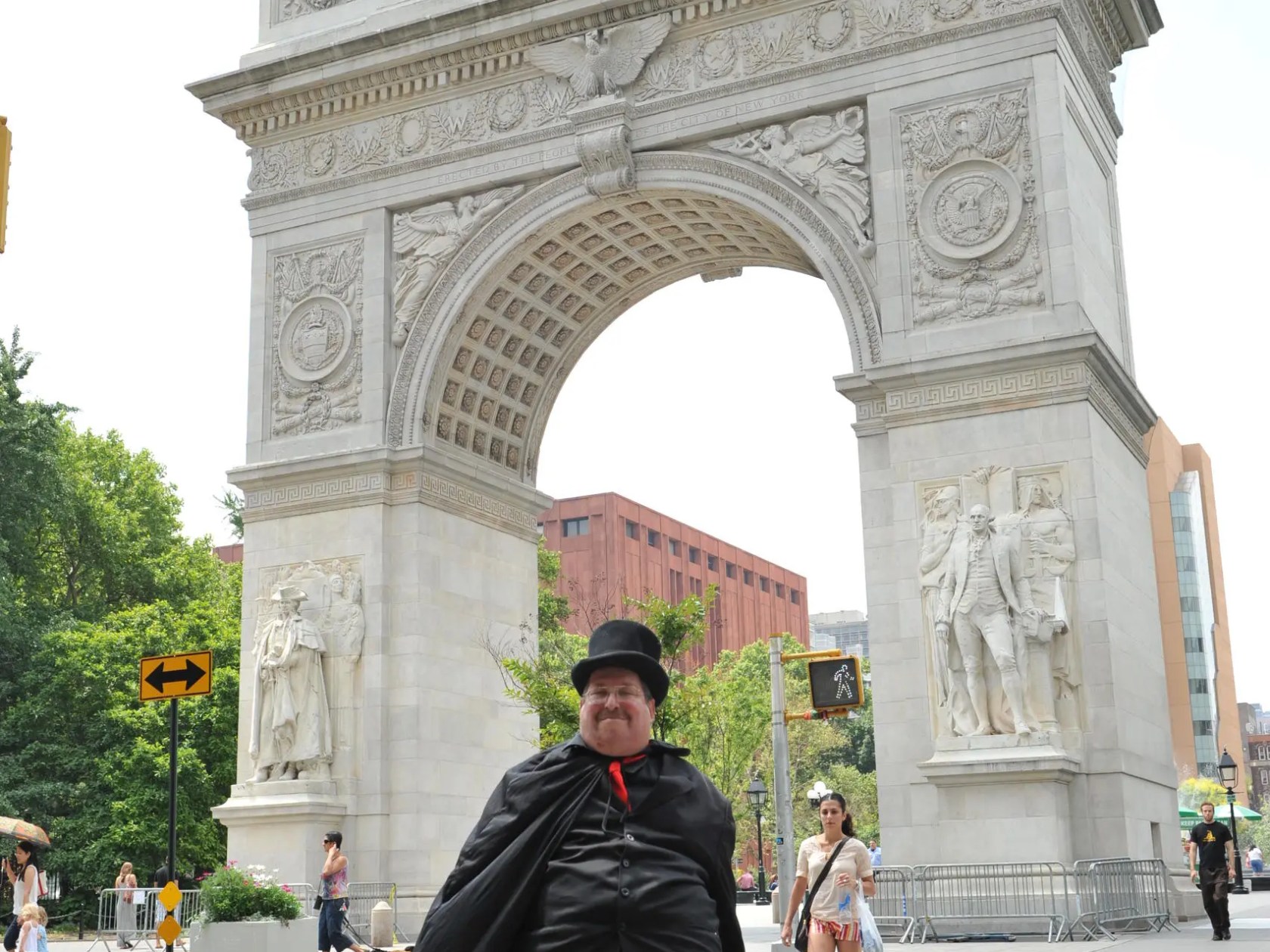 Person in costume stands beneath an ornate archway sculpture on a city street.