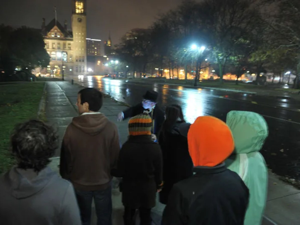 People in coats gathered on a sidewalk at night near a lit building.