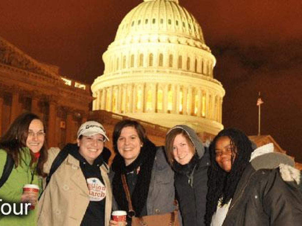 Five people smiling in front of the U.S. Capitol at night.