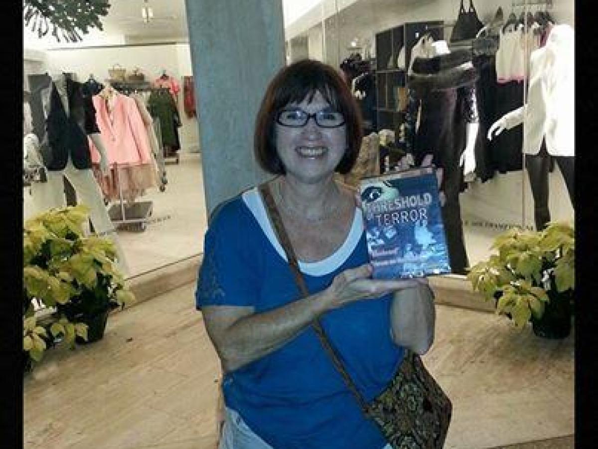 Smiling woman holding book, standing in a mall. Text: Ghosts of Palm Beach Trivia Challenge Winner.