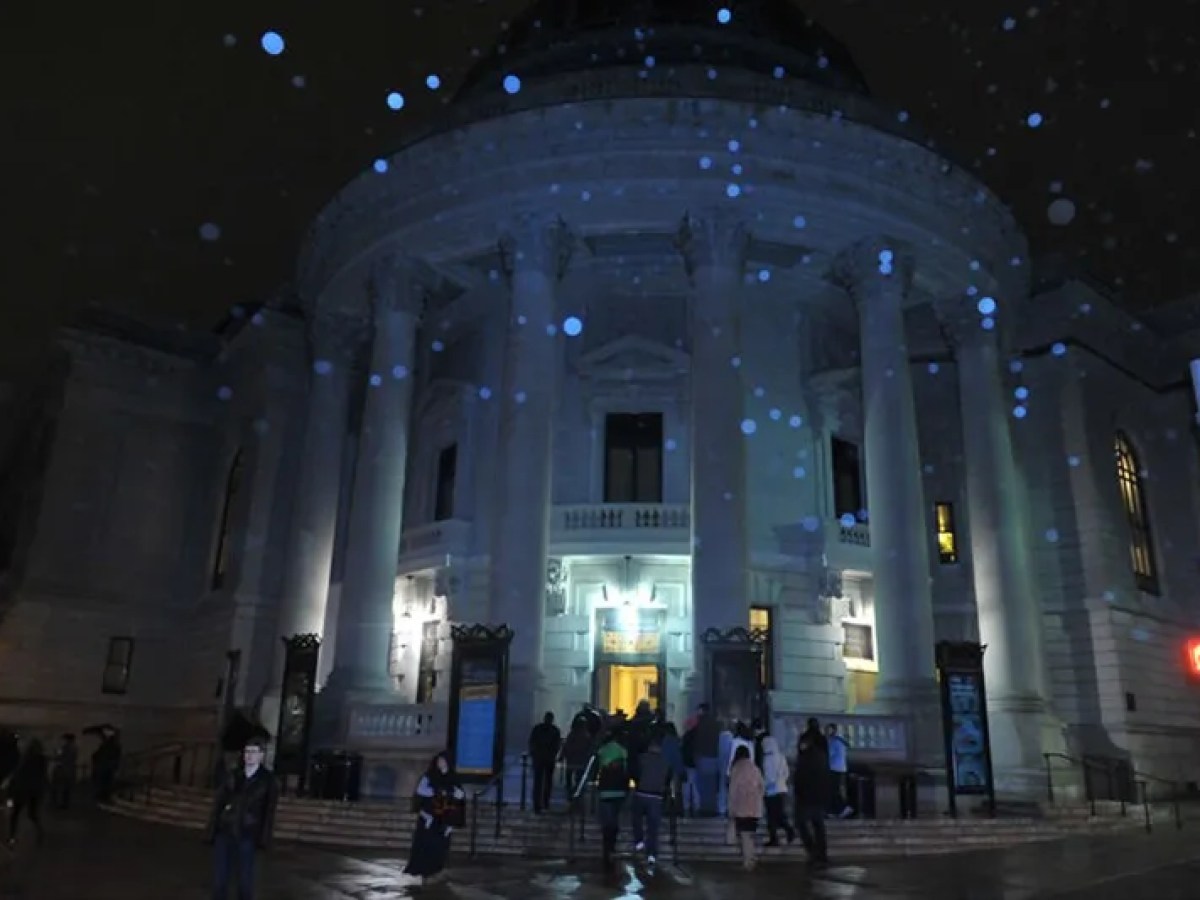 People entering a lit, dome-shaped building at night with rain droplets visible.