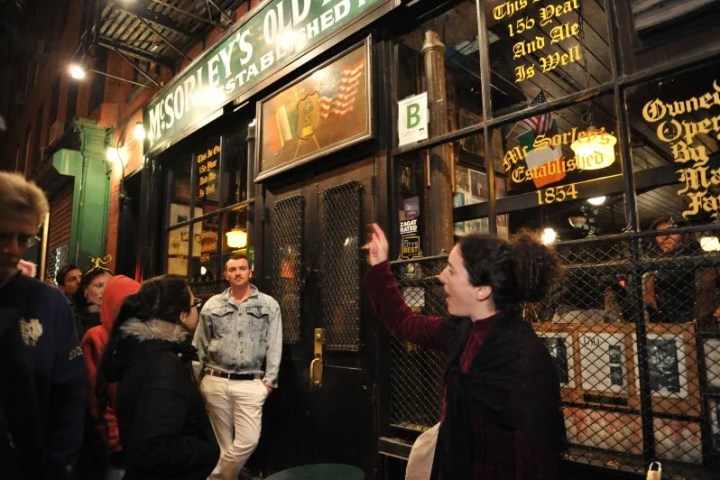 People stand outside McSorley's Old Ale House at night, under a lit sign.