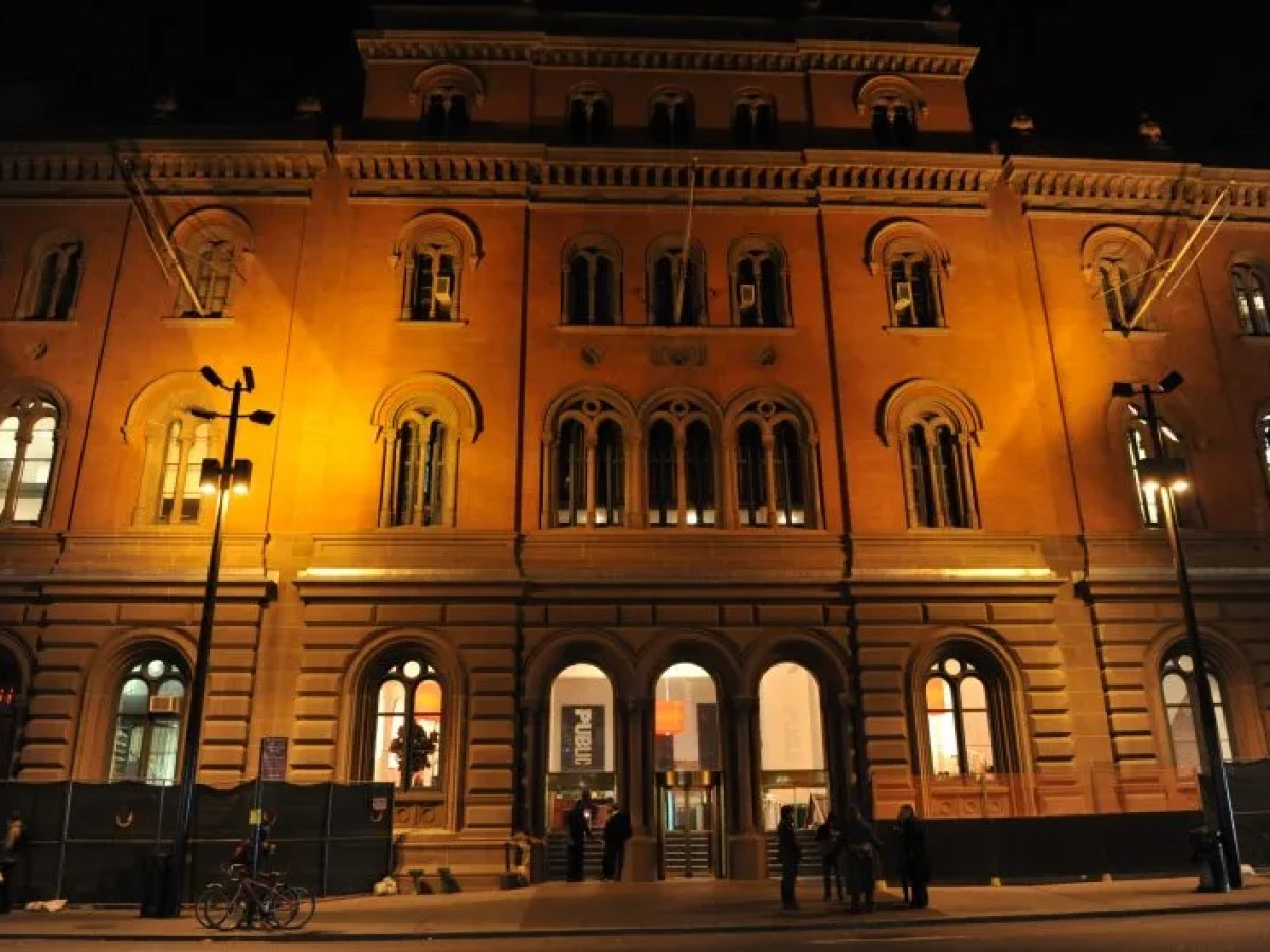 Illuminated historic building facade at night with arched windows and street lamps.