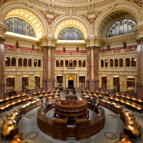 Ornate library interior with arched ceiling, desks, and statues.